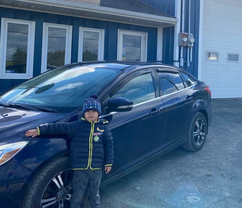 A young boy stands in front of a car.