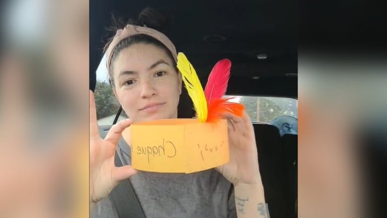 A woman in a car holds up a cardboard headdress with fake feathers.