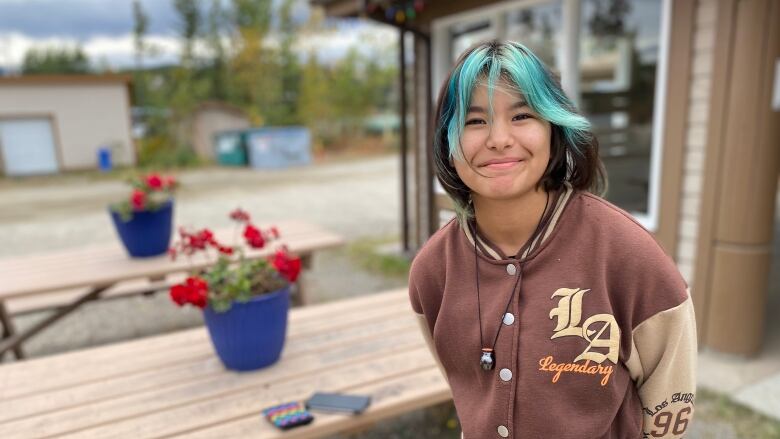 A young person with green and black hair smiles at the camera.