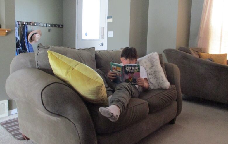 A young boys reads a book on a sofa.