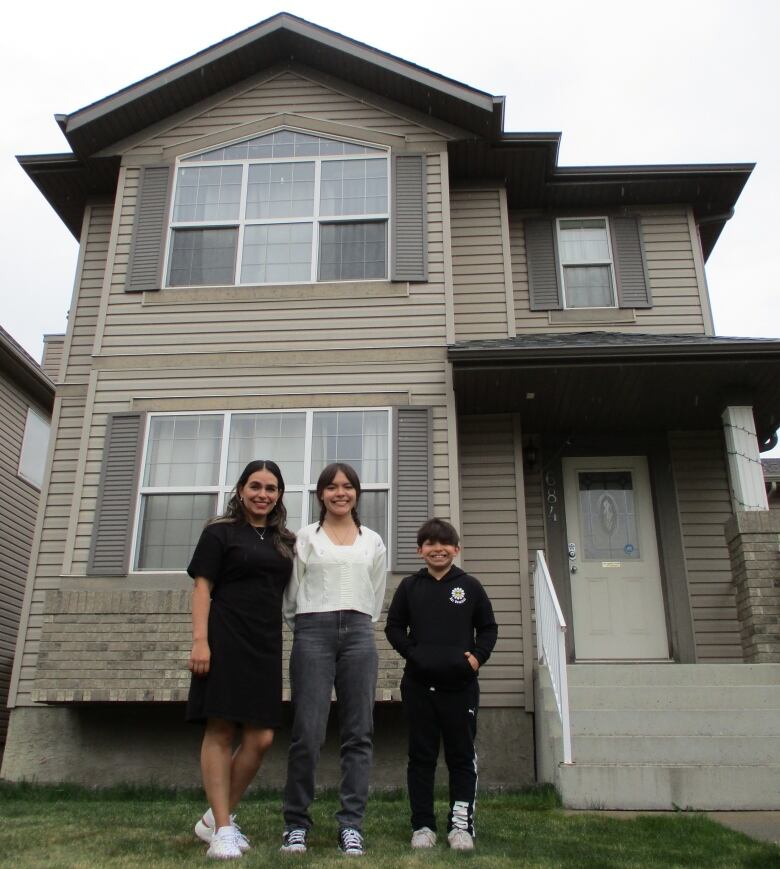 A woman with two children stand in front of a house.