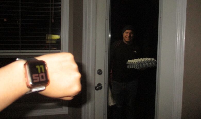 A man carrying a flat of eggs stands in the dark at a door.