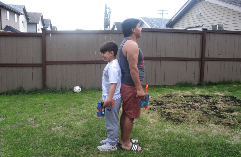 A man and his son stand back to back with nerf guns.