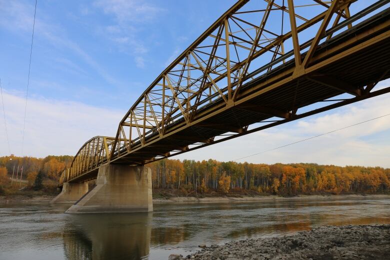 A yellow bridge is shown amid fall foliage and a blue sky.