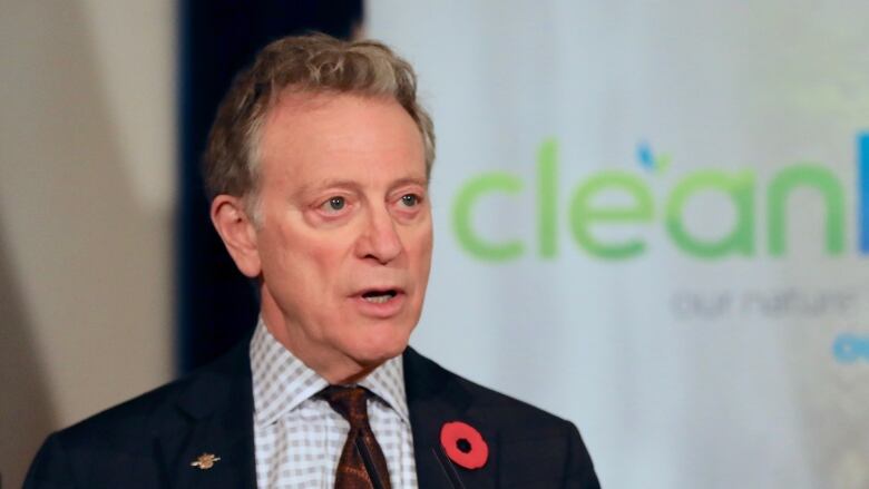 George Heyman, a white man wearing a poppy and a suit, poses at a podium in front of a 'CleanBC' banner.