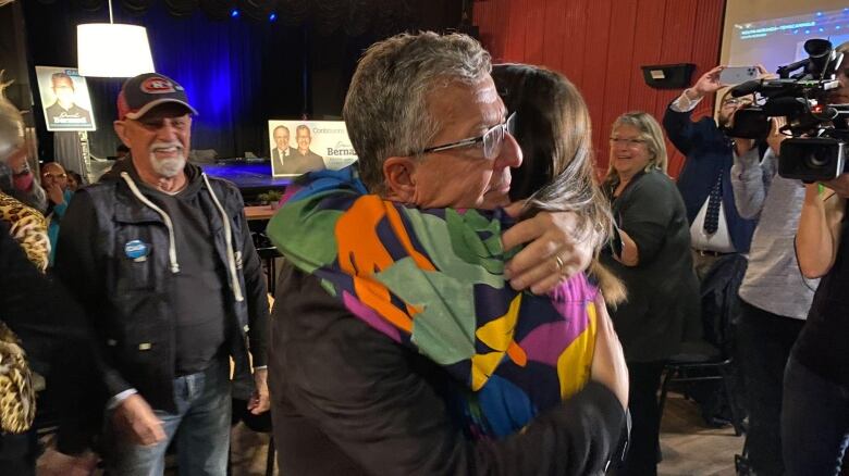 A man hugging a woman in front of a crowd of people and cameras.