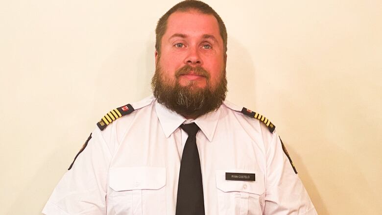 A man with grey-green eyes is seen wearing an uniform of a white shirt and black tie, with 'fire chief' badges on his shoulders.