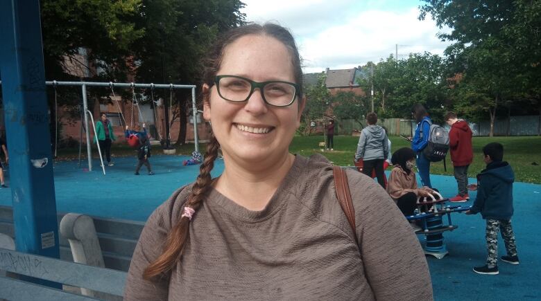 A woman smiles at the camera. Her hair is in a braid and she is wearing a brown shirt and glasses.