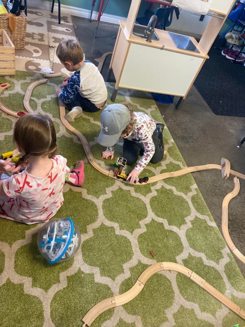 Toddlers play with toys on a rug.