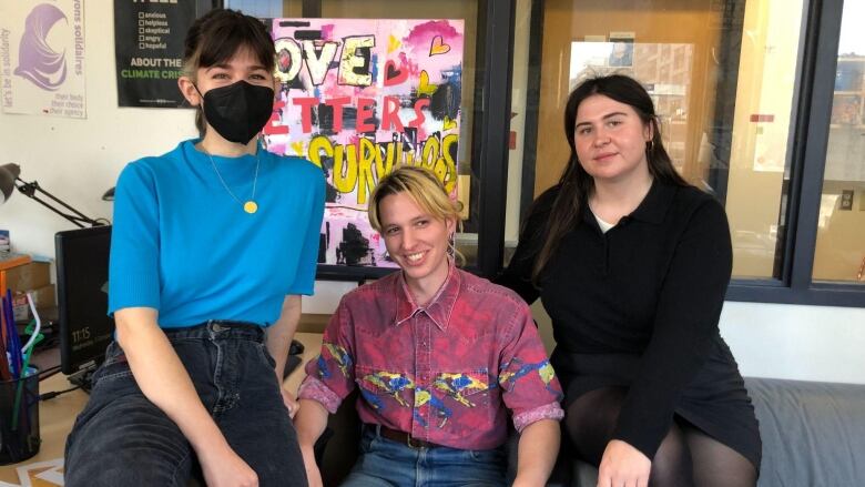 three people sitting on a couch in front of a poster saying 