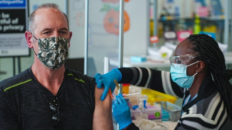 A nurse uses a needle to deliver COVID vaccine to a man.