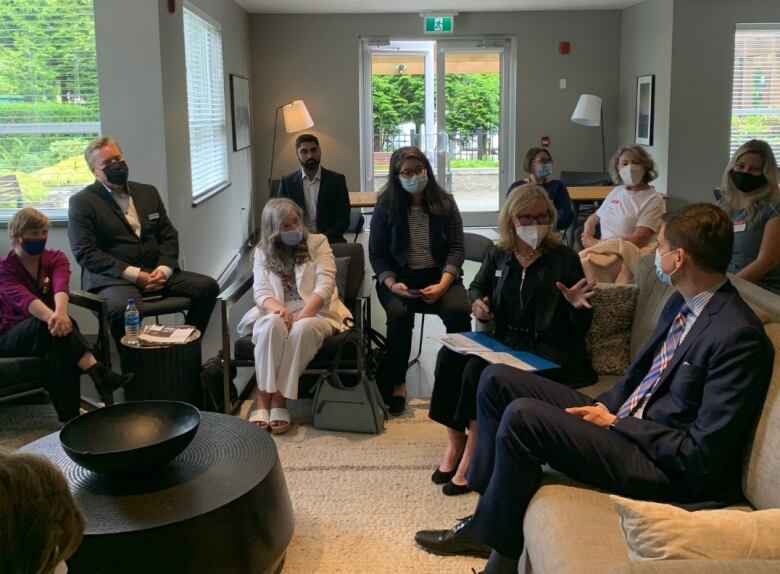 David Eby, a man in a suit, listens to a group of people in a small room.