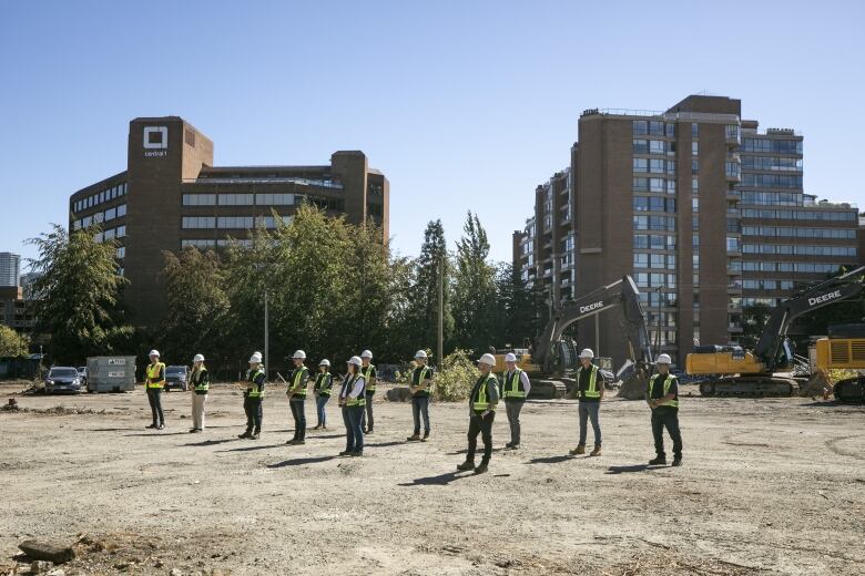 People in hard hats and hi-viz vests stand in a dirt lot during a groundbreaking ceremony for the Senakw development in Vancouver.