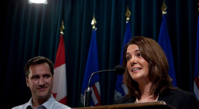 A man looks at a woman speaking into the microphone to his left.