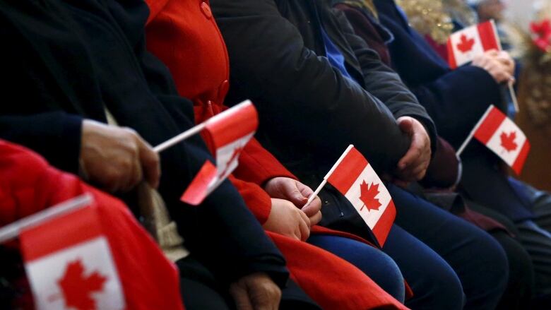 A line of seated people clutch small Canadian flags. 