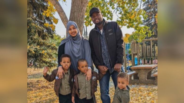 A family of five standing in a park.