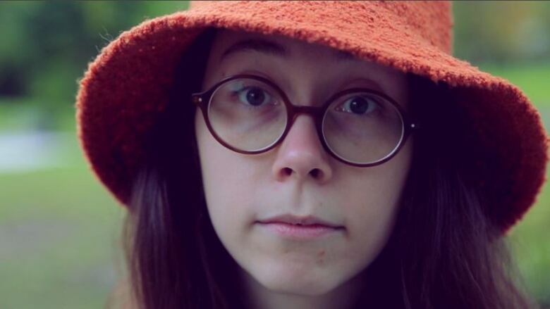 A woman wears a large orange woolen hat and round glasses. 