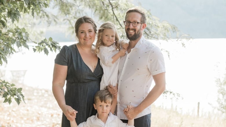 A smiling family poses for a photo against the backdrop of a lake. 