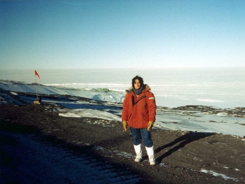 A woman in a red parka poses in front of a barren snowy landscape.