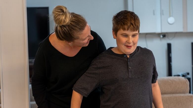 A young boy with short brown hair laughs as a woman looks on.