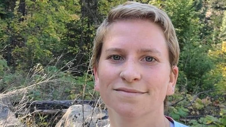 A woman takes a selfie with a forest as her background.