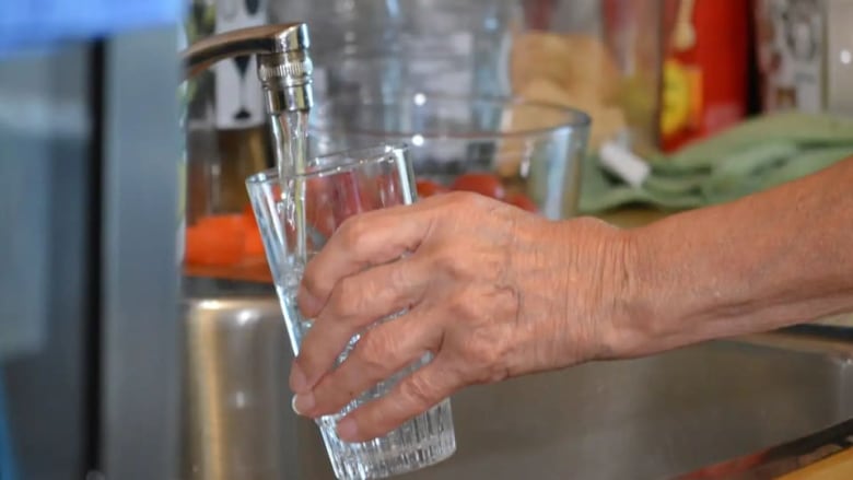 A hand fills a glass of water at a faucet. 