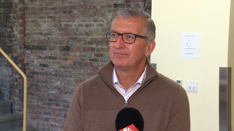 A man wearing glasses stands in front of a brick wall.