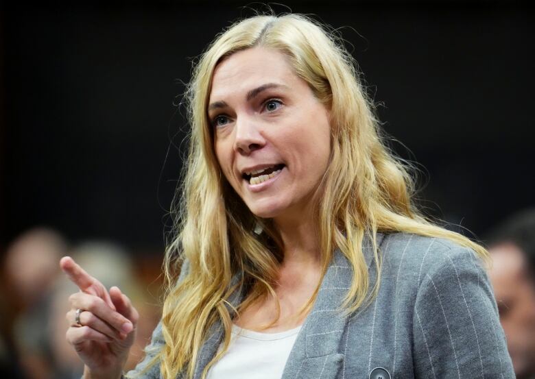 A woman in a suit points while speaking. 