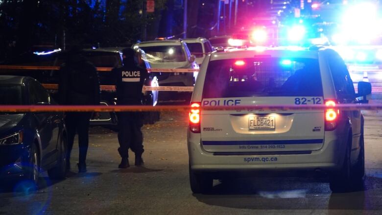 Montreal police officers stand beside a parked police car. 