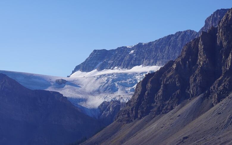 A large glacier hugs the side of a mountain against a blue sky.