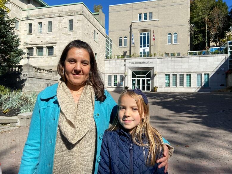 A mother and daughter stand in front of a school.