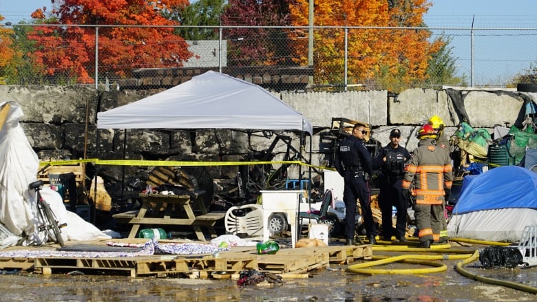 Police officers and firefighters gather beside a structure that was on fire.