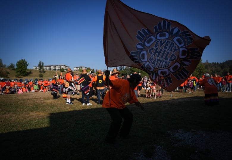 A man waves an Every Child Matters flag as First Nations drummers sing and drum during a ceremony to mark the National Day for Truth and Reconciliation, at the site of the former St. Mary's Indian Residential School in Mission, B.C., on Fri. Sept. 30, 2022.