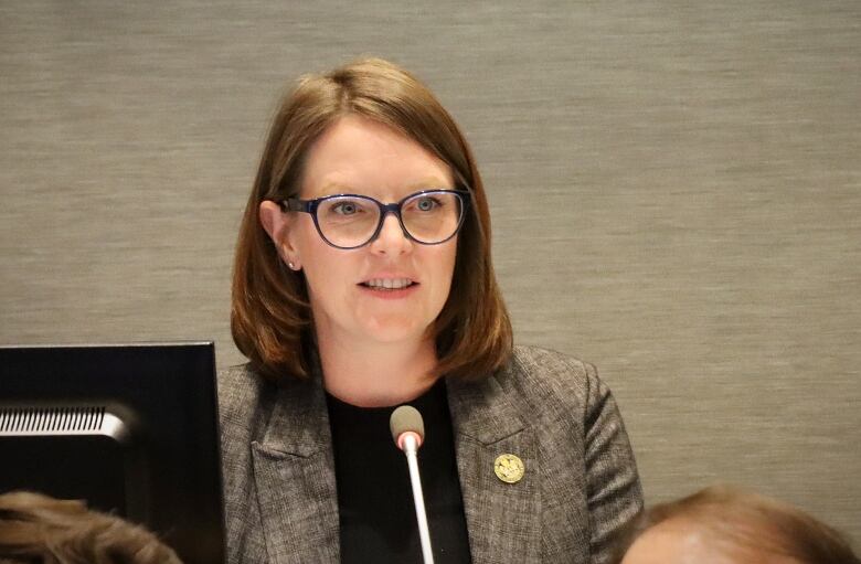 A woman in glasses sits and speaks.