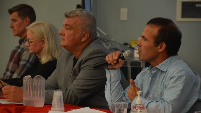 Four mayoral candidates sit at a table, with Ozzie Grandinetti speaking into a microphone.