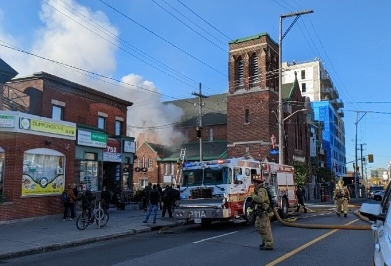 People stand across the street from a church with smoke coming from it.