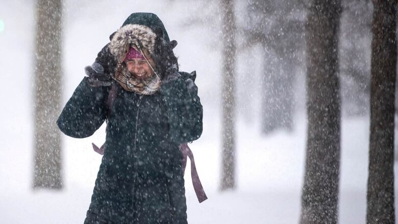 A person holds their hood up while walking in the snow.