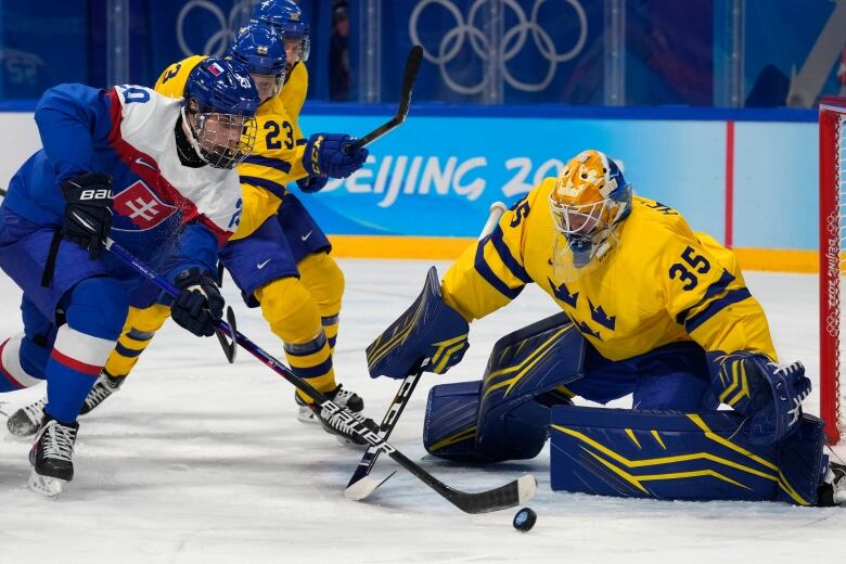 A skater in blue tries to take a shot against a goalie in yellow.