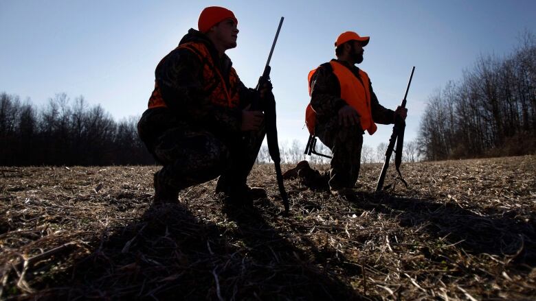 Two hunters, kneeling, with their rifles pointed in the air.