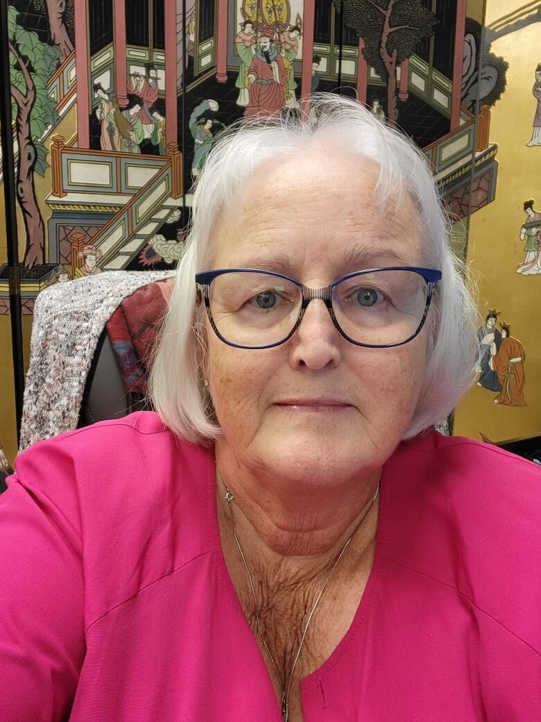 A woman in her sixties wearing a pink shirt smiles. 