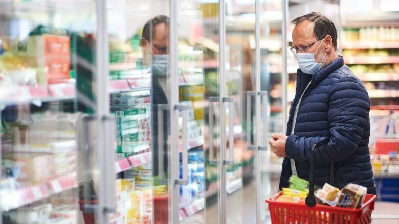 Man holds grocery basket, he is wearing a mask.