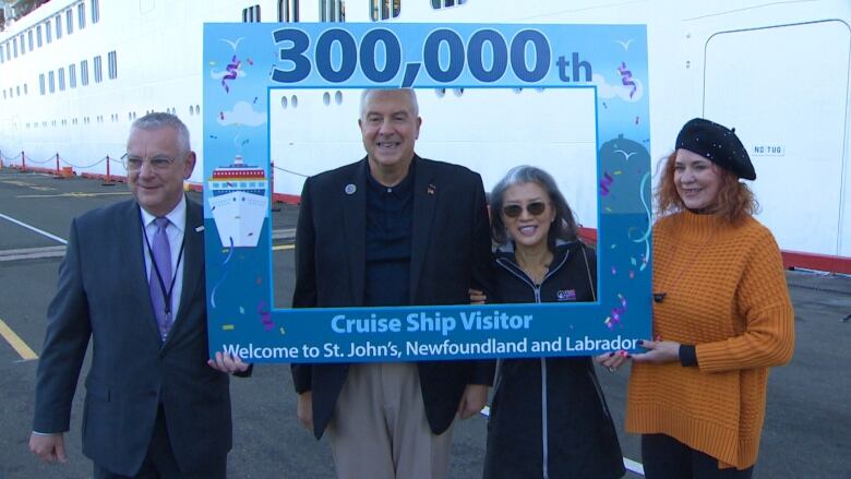 City officials hold a frame that reads 300,000th cruise ship visitor while a man and woman stand in the middle. 