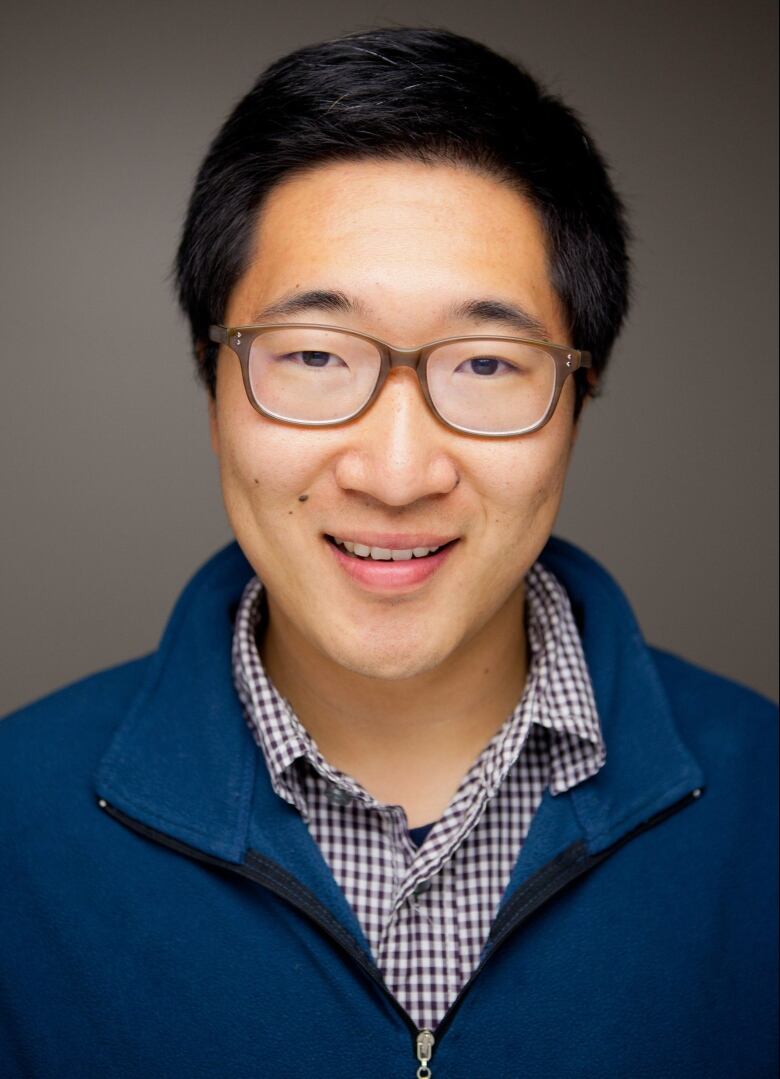 A headshot of a man wearing a blue shirt and half zipped sweater.