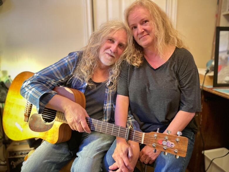 A woman and man smile for the camera while the man holds a guitar.