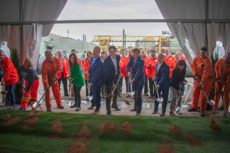 A line of people learn forward while holding shovels with dirt.