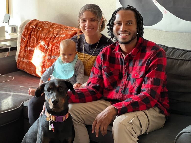 A man, woman and a baby sit on a couch in a living room.