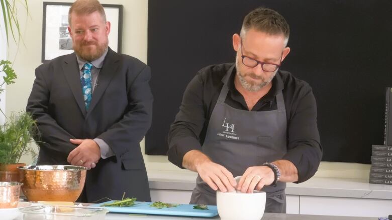 A chef places food in a white bowl while another looks on.