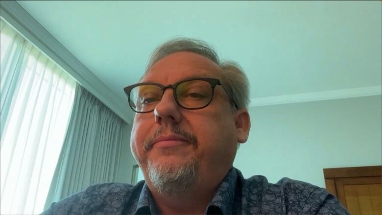 A man sits in a hotel room on a Zoom video call.