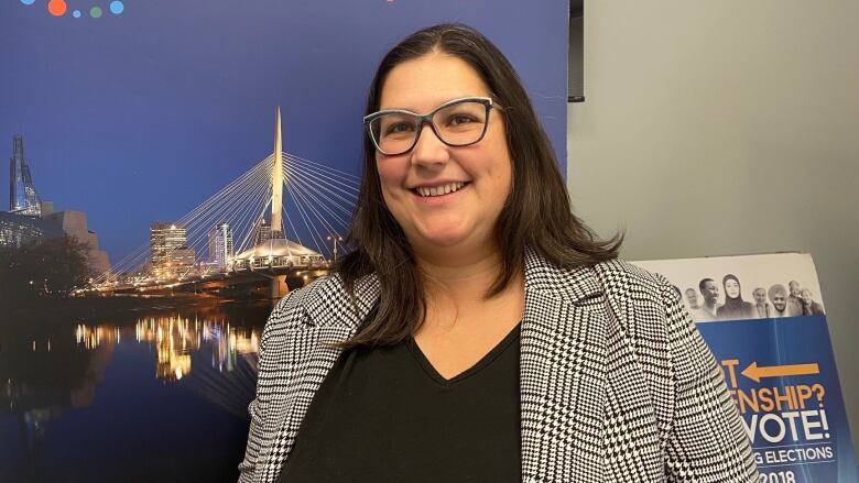 A woman with glasses smiles in front of a picture of Winnipeg's skyline.