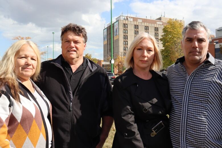 Two couples stand side by side, outside of a hospital. 